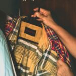 Osoba trzyma w szafie męską koszulę w kratę na wieszaku